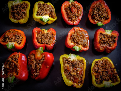 Canvas Print Red and yellow bell peppers cut in half, filled with minced beef meat and baked,
