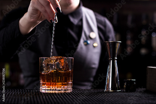 Bartender making refreshing coctail on a bar background. Dark moody style. Ice in tha glass