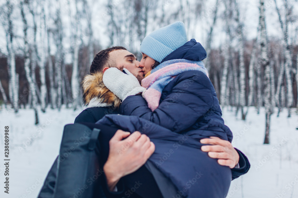 Guy carrying his girlfriend on hands and kissing in winter forest. People having fun outdoors Guy carrying his girlfriend on hands and kissing in winter forest. People having fun outdoors