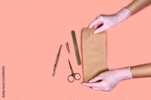 packing a manicure tool in kraft packages before sterilizing in a dry oven. Manicure tool in the hands of the master isolated on pink background. the concept of healthy manicure © Надія Коваль