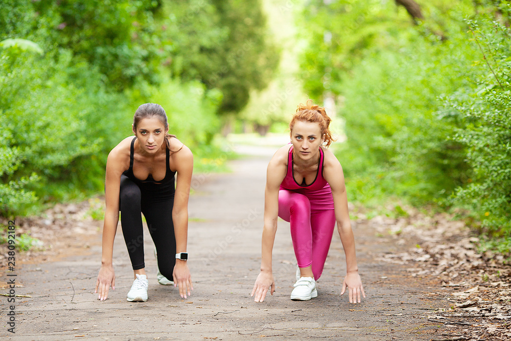 Fitness. Two female runners stretching legs outdoors in park in summer Fitness. Two female runners stretching legs outdoors in park in summer