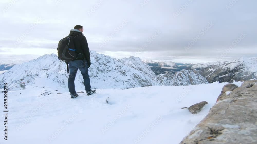 Tourist with backpack stands on mountain looking at snow covered landscape Tourist with backpack stands on mountain looking at snow covered landscape