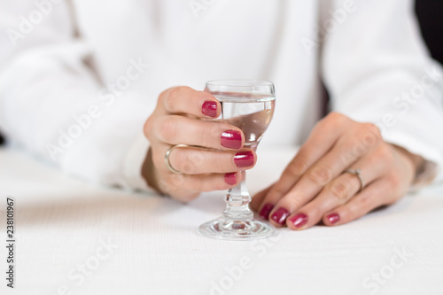 Kobieca dłoń z umalowanymi na czerwono paznokciami trzyma kieliszek wypełniony wódką.
