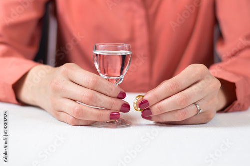 Kłopoty małżeńskie. Kobieta trzyma w jednej dłoni złotą obrączkę ślubną a w drugiej kieliszek z wódką. 