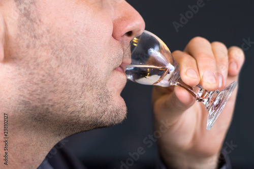 Biały mężczyzna trzyma kieliszek do wódki przystawiony do ust i pije wódkę.