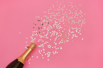 Champagne bottle with confetti stars on pink background. Copy space, top view