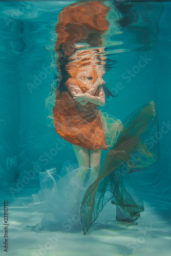beautiful model girl swims underwater in orange dress and enjoys relaxation and lack of stress