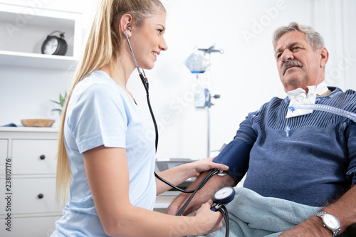 young pretty blonde nurse nurses an elderly patient in the hospital and measures his blood pressure with a cuff and prepares to inject with a syringe photo