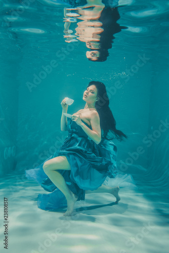 funny girl having fun and drinking soothing tea for Breakfast while meditatively swimming underwater in a dress