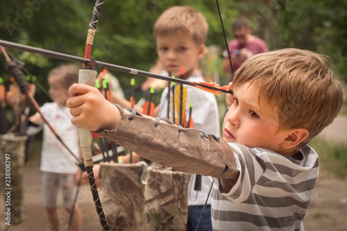 Boy with bow and arrow concentrated on target. Kid stared at target. Child directed arrow at a target. Bowman background. Children and sports. Physical training. Alternative schooling.