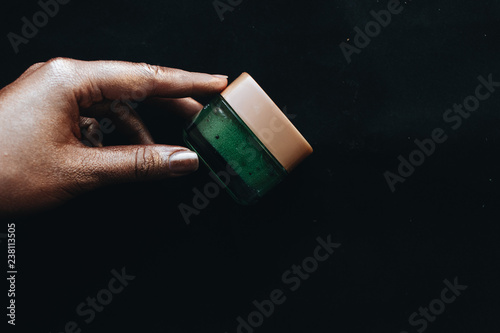 Female hand holding container with green cream on black background