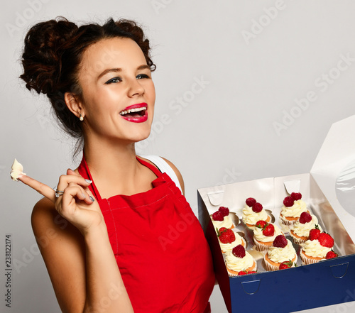 Young woman chef cook hold sweet cup cakes box with cream happy surprised on gray