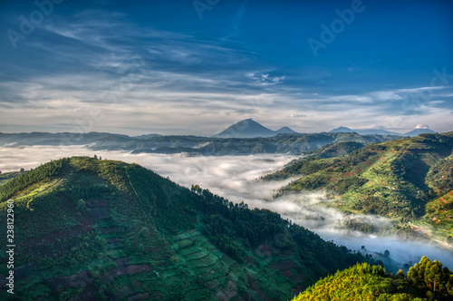 Morning in Uganda with volcanoes in background, fog in the valley and farmlands stretching far
