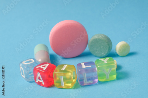 Word DAILY from the letters of cubes and medical pills. Colored pills and capsule on blue background. Pharmacy Theme,