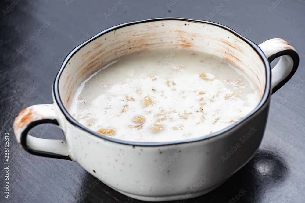 Morning Breakfast, oatmeal on milk with butter in white plate on dark background Morning Breakfast, oatmeal on milk with butter in white plate on dark background