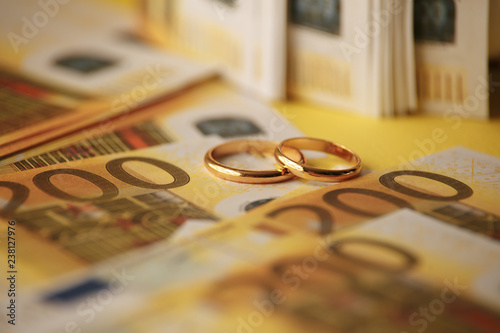 Two wedding rings and money as symbol for an expensive alliance. Golden wedding rings on euro banknotes background. Marriage of convenience