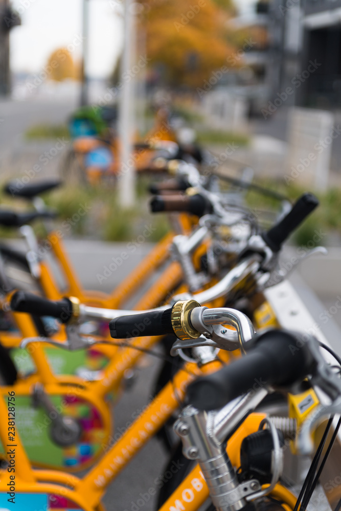 Miet-Fahrräder an einem Fahrrad-Ständer in der Innenstadt mit Fokus auf einen Lenker Miet-Fahrräder an einem Fahrrad-Ständer in der Innenstadt mit Fokus auf einen Lenker