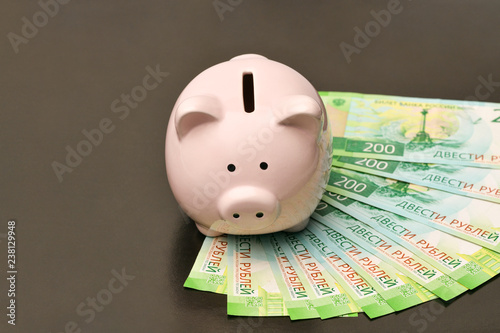 Pink piggy Bank in shape of pig is standing in the center on black brown background underneath lcat Russian rubles par value of two hundred rubles. black Friday photo