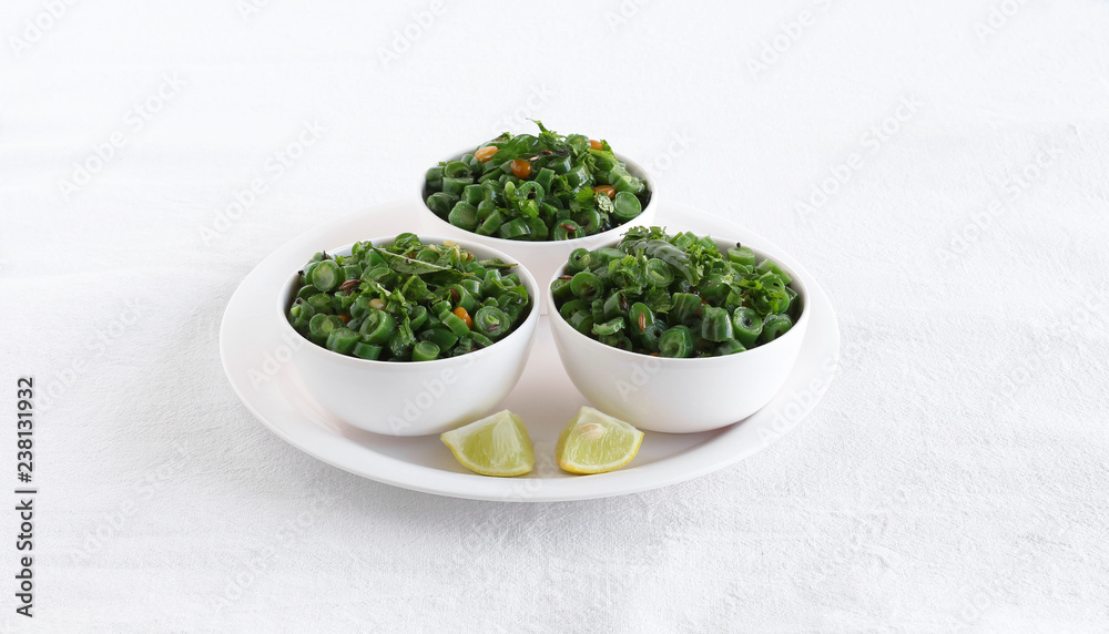Green bean curry, a south Indian traditional and popular vegetarian side dish in three bowls on a plate with lemon slices. Green bean curry, a south Indian traditional and popular vegetarian side dish in three bowls on a plate with lemon slices.