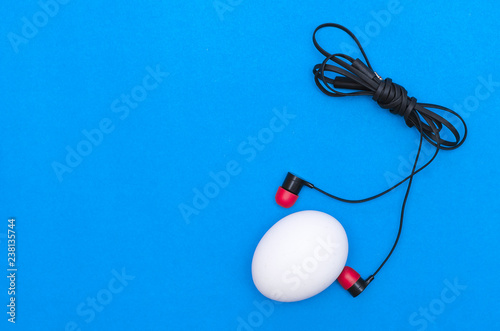 Chicken egg and headphones isolated on blue background. Abtract photo.