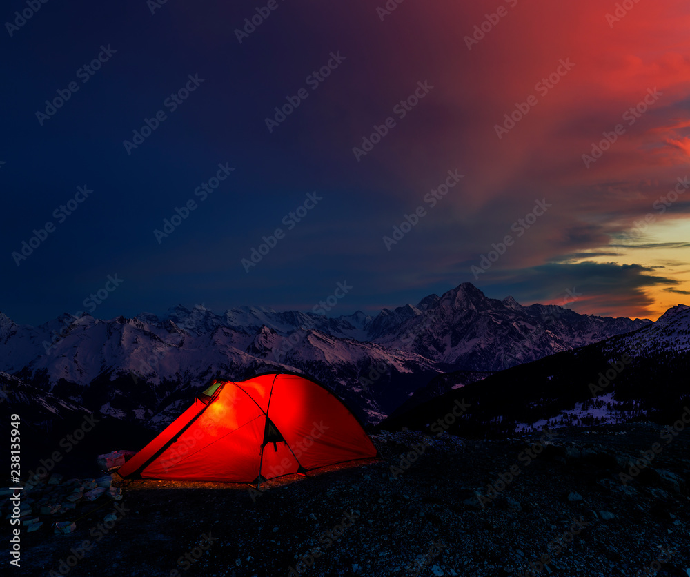 Night bivouac in Mountains, milion star hotel under night sky, red illuminated tent on pass in Alps.