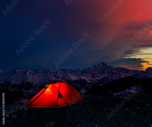 Night bivouac in Mountains, milion star hotel under night sky, red illuminated tent on pass in Alps. photo