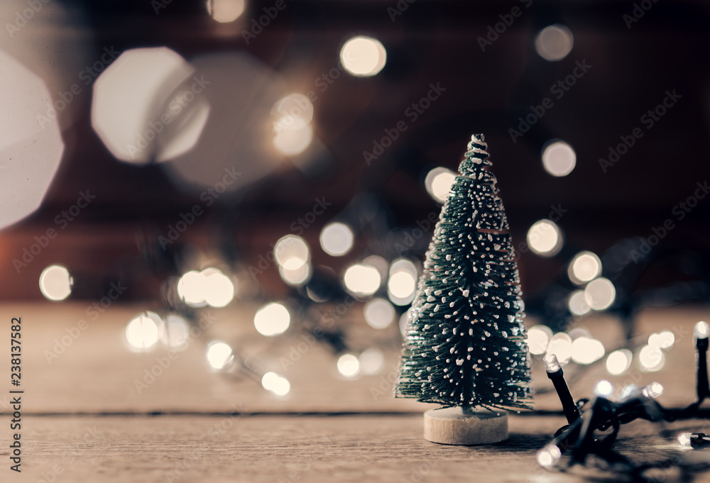 Christmas decorations on wooden table with glowing lights. A small artificial Christmas tree and an electric garland.