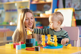 Cute woman and kid toddler boy playing educational toys at kindergarten or nursery room
