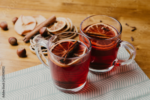 Mulled wine in mugs with scarf on wooden table.