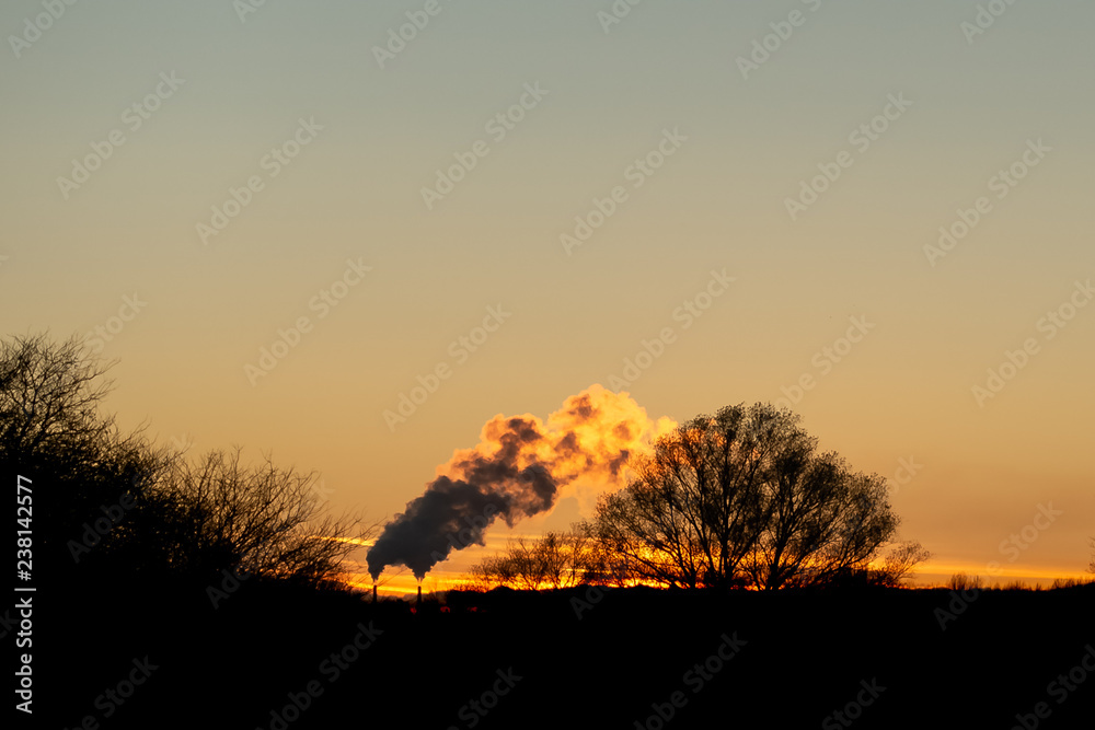 Fototapeta premium Sun setting over smoke from factory - orange look