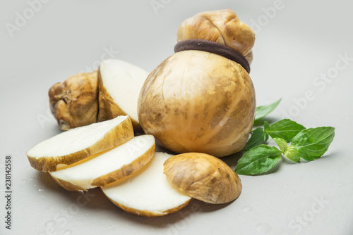 Traditional Italian smoked Scamorza cheese with herbs on gray background.
