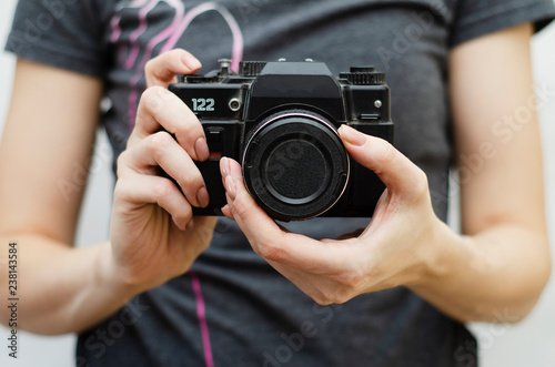 a girl in a gray t-shirt holding an old camera in her hands on a light background