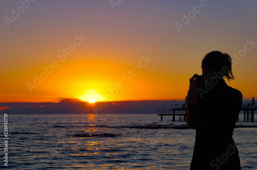 A young woman photographs an amazing sunset on the sea in the evening.