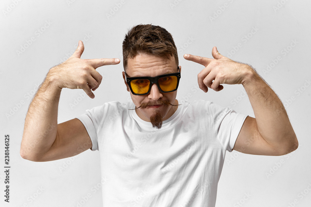 Style, fashion, masculinity and confidence concept. Picture of self  confident stylish young beard man in yellow tinted computer glasses in  rectangular black frame, pointing fore fingers at his head Stock Photo