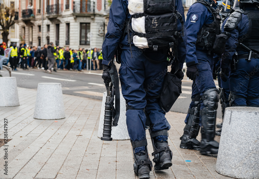 Rear view of police officers securing the zone in front of the Yellow vests movement protesters on Quai des Bateliers street detail on their guns, rifles, baton, gas tear guns, Rear view of police officers securing the zone in front of the Yellow vests movement protesters on Quai des Bateliers street detail on their guns, rifles, baton, gas tear guns,