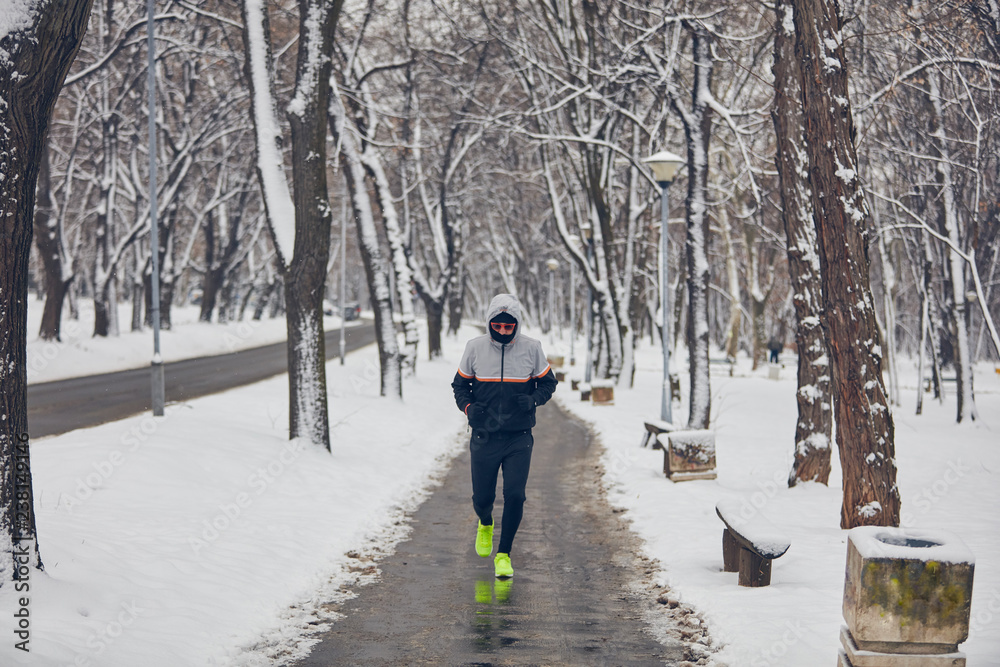 Man jogging in a cold winter snowy day outdoors.