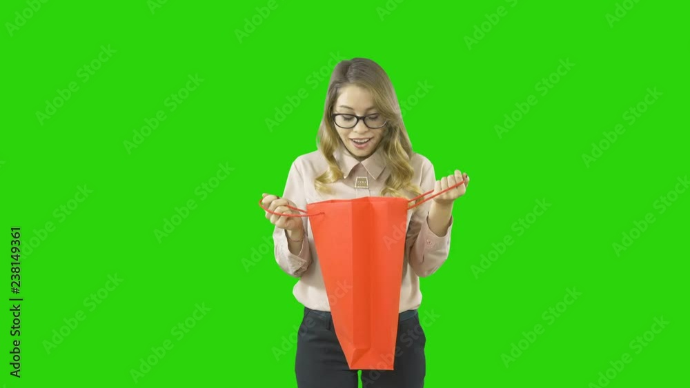 A girl in a strict suit inspects her New Year's gift by opening the package and took out a box opened and genuinely rejoiced, filming on an isolated green background A girl in a strict suit inspects her New Year's gift by opening the package and took out a box opened and genuinely rejoiced, filming on an isolated green background