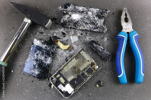 shattered, broken smartphone and hammer on gray background