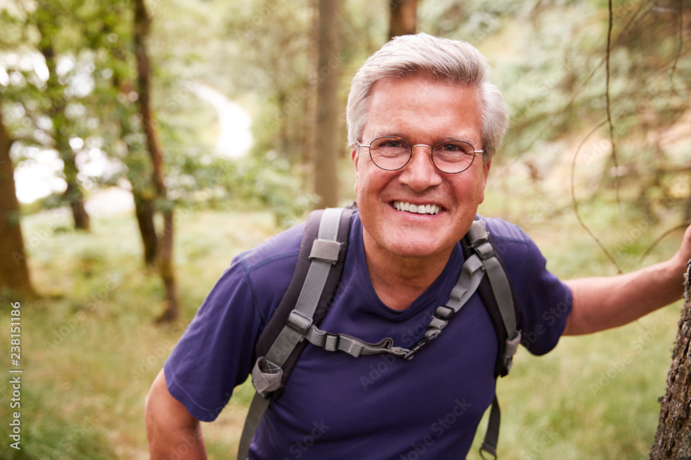 Middle aged Caucasian man taking a break leaning on a tree during a hike in a forest, smiling to camera, close up Middle aged Caucasian man taking a break leaning on a tree during a hike in a forest, smiling to camera, close up