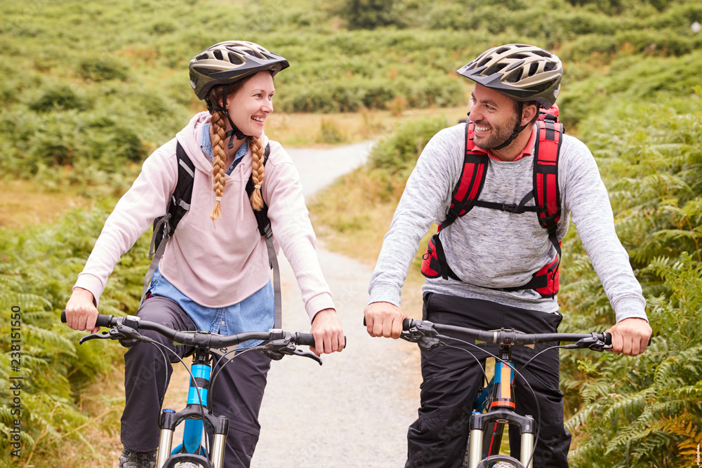 Φωτογραφία Young adult couple riding mountain bikes in a country lane, looking each other,