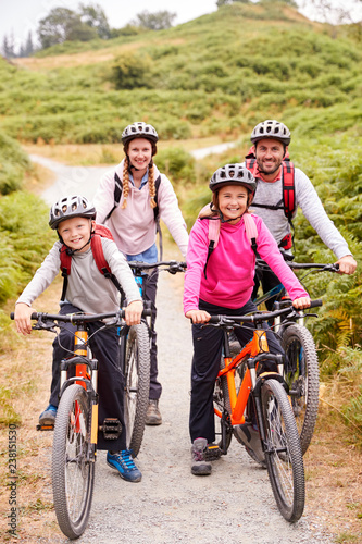 Parents and children sitting on mountain bikes in a country lane during a family camping trip, full length