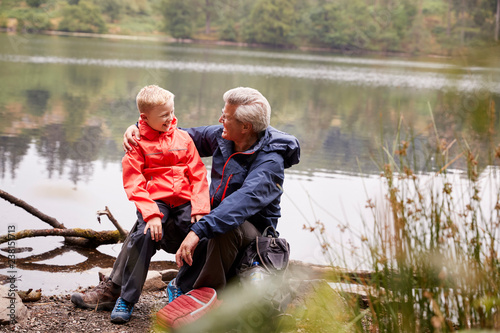Grandson sitting on his grandfather's knee at the shore of a lake, Lake District, UK