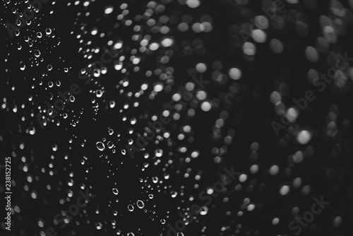 Dirty window glass with drops of rain. Atmospheric monochrome dark background with raindrops in bokeh. Droplets and stains close up. Detailed transparent texture in macro. Copy space. Rainy weather.