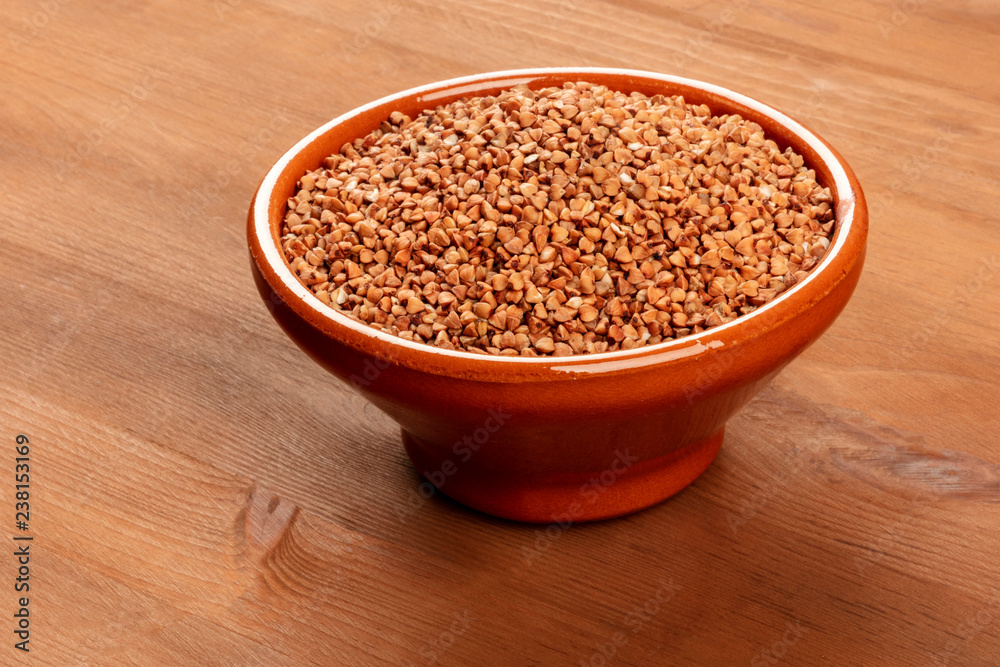 A photo of raw buckwheat in an earthenware bowl on a dark rustic wooden background with copy space A photo of raw buckwheat in an earthenware bowl on a dark rustic wooden background with copy space