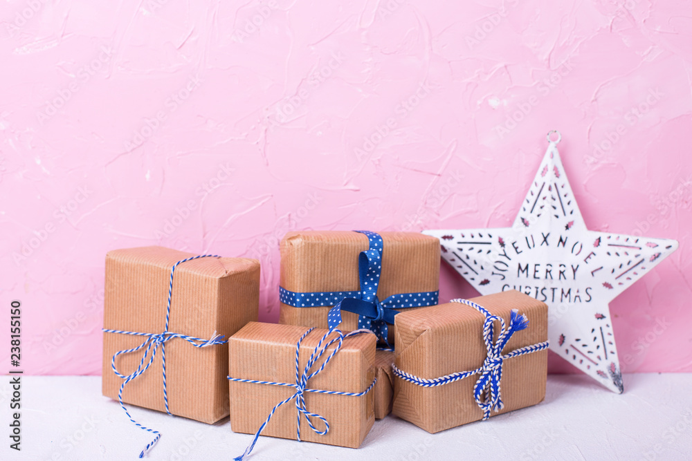 Wrapped boxes with presents and Christmas star on white textured background against pink wall. Wrapped boxes with presents and Christmas star on white textured background against pink wall.