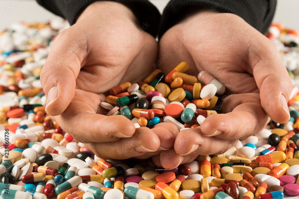 Male hands holding high number of  pills on white blackground. High resolution image for pharmaceutical industry.