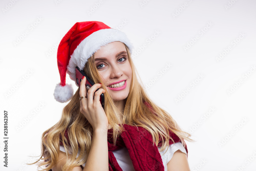 Attractive smiling woman in red Santa hat talking on the phone and looking at the camera. Christmas, new year and celebration