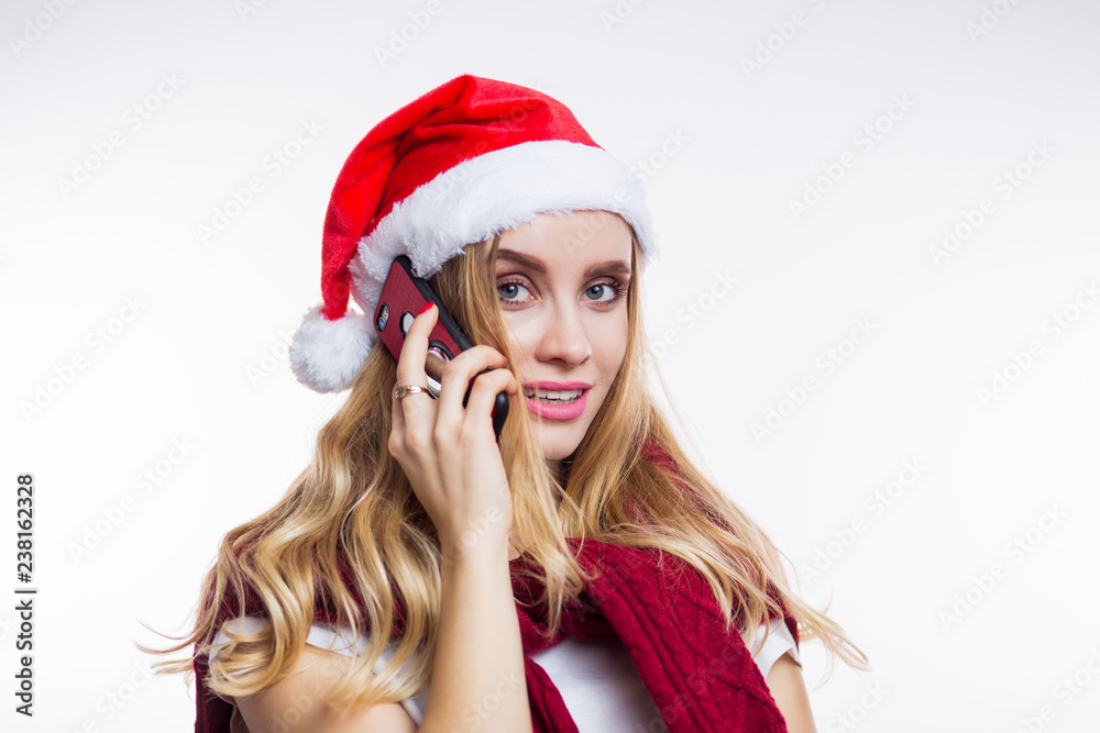 Cheerful happy woman puts on Santa's red hat and talks on her smartphone. Online shopping, Christmas discounts, gift shopping, Christmas Cheerful happy woman puts on Santa's red hat and talks on her smartphone. Online shopping, Christmas discounts, gift shopping, Christmas