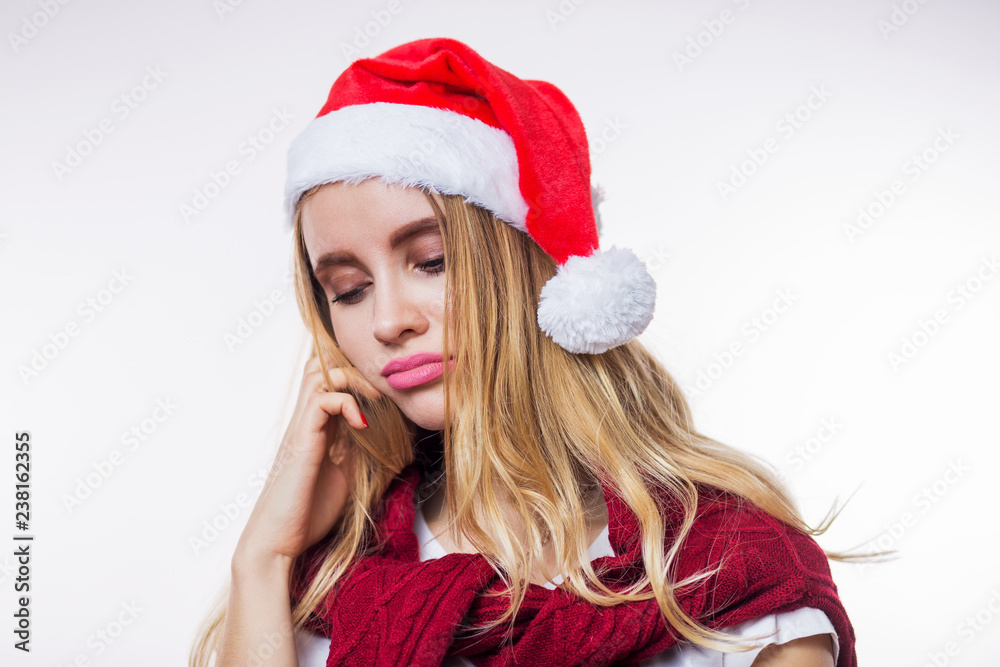 Closeup portrait of sad upset beautiful blonde woman wearing red Santa hat on white background. Bad mood, disappointment in the new year. Expressive facial expressions Closeup portrait of sad upset beautiful blonde woman wearing red Santa hat on white background. Bad mood, disappointment in the new year. Expressive facial expressions
