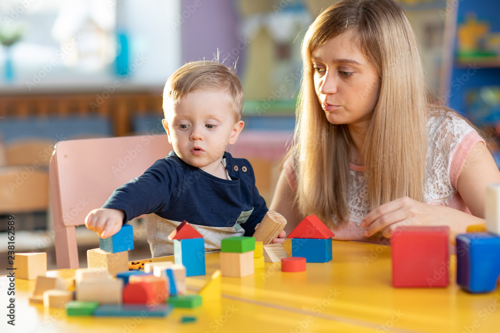 Cute female teacher and child toddler boy playing educational toys in kindergarten or nursery Cute female teacher and child toddler boy playing educational toys in kindergarten or nursery
